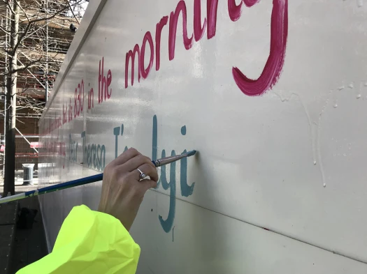 Francesca painting coloured words onto the hoardings